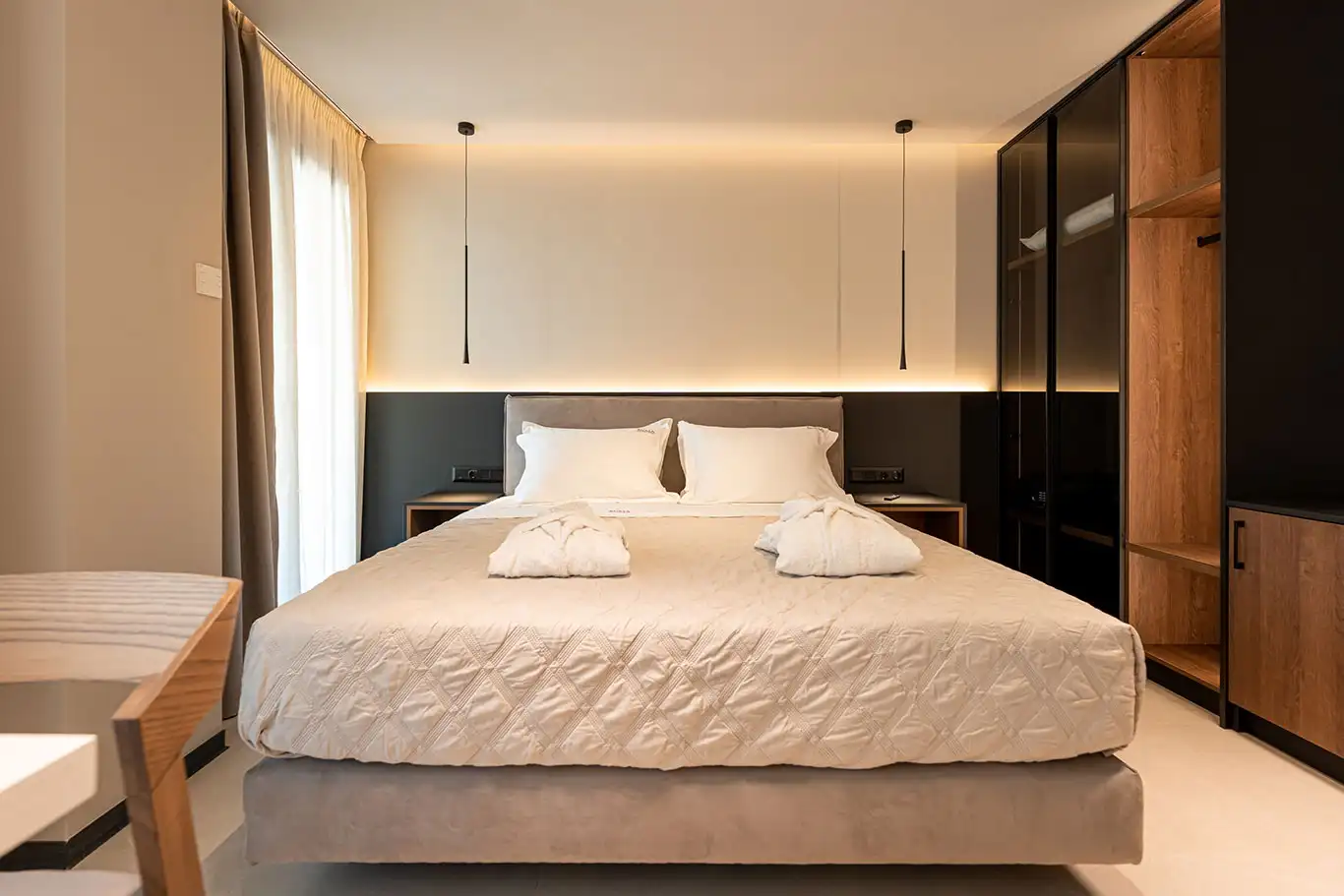 Bright double bedroom with white bedding, folded bathrobes, pendant lights and built-in wardrobe
