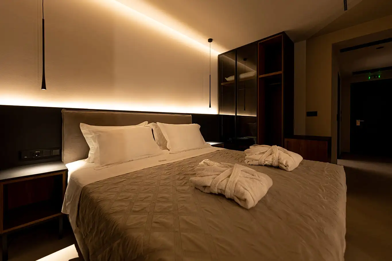 Double bed with white pillows, folded bathrobes, bedside tables and illuminated wardrobe