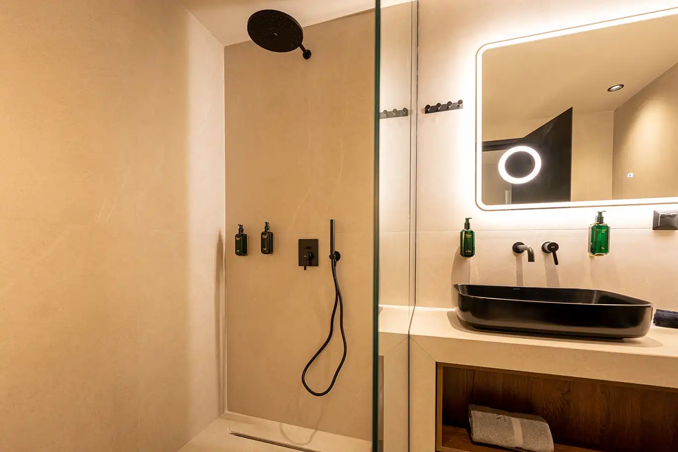 Modern bathroom with black basin, illuminated mirror and glass walk-in shower with rainfall showerhead