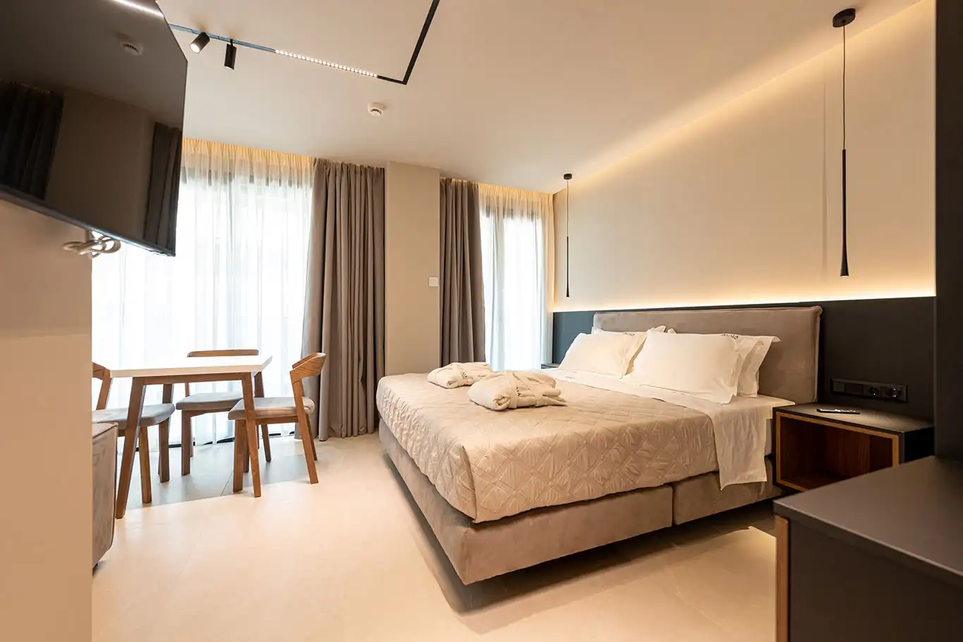 Spacious double bedroom with folded bathrobes, dining table, wall-mounted television and large windows