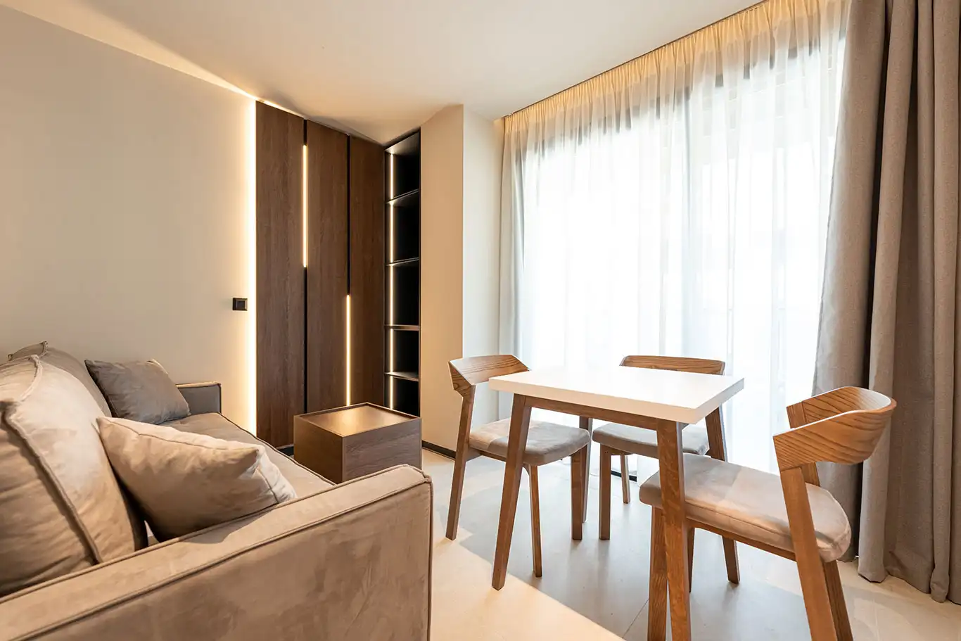 Bright living area with beige sofa, wooden coffee table, white dining table and floor-to-ceiling curtains