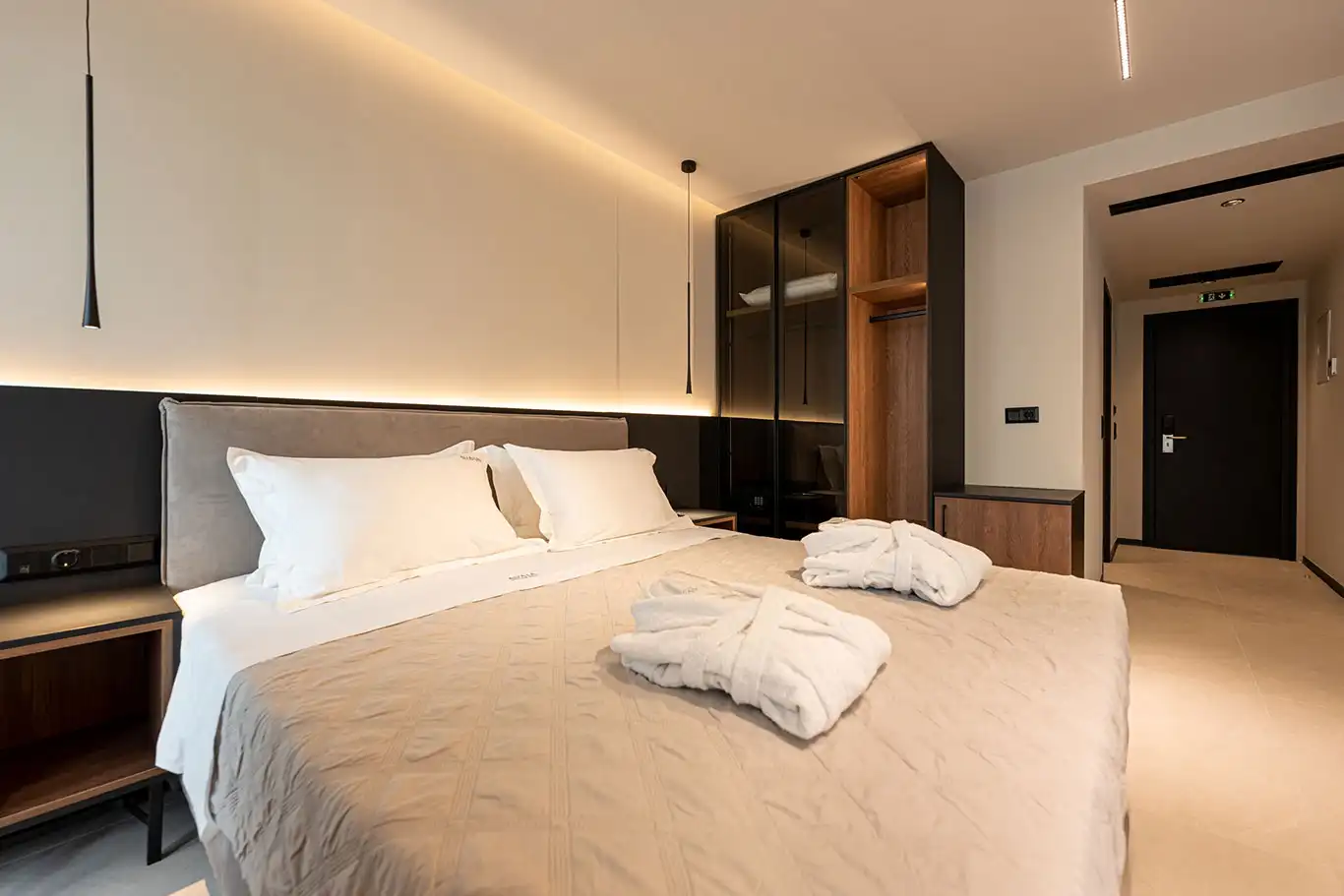 Double bed with white bedding, folded bathrobes, bedside tables and illuminated built-in wardrobe