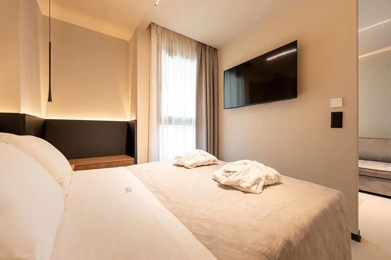 Double bed with folded bathrobes, wall-mounted television, floor-to-ceiling curtains and access to the living area