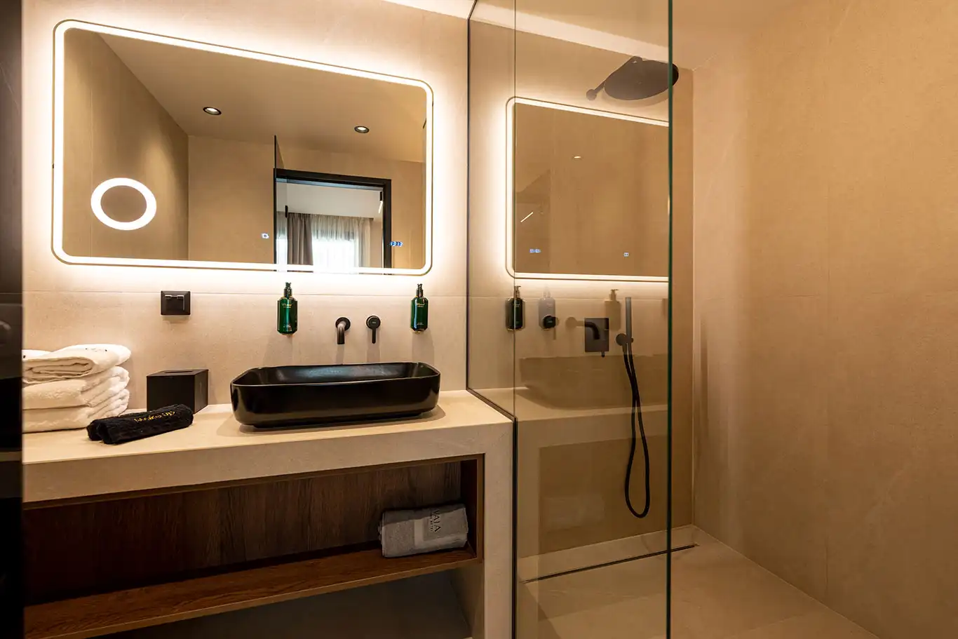 Modern bathroom with black basin, illuminated mirror and glass walk-in shower with matte black fixtures