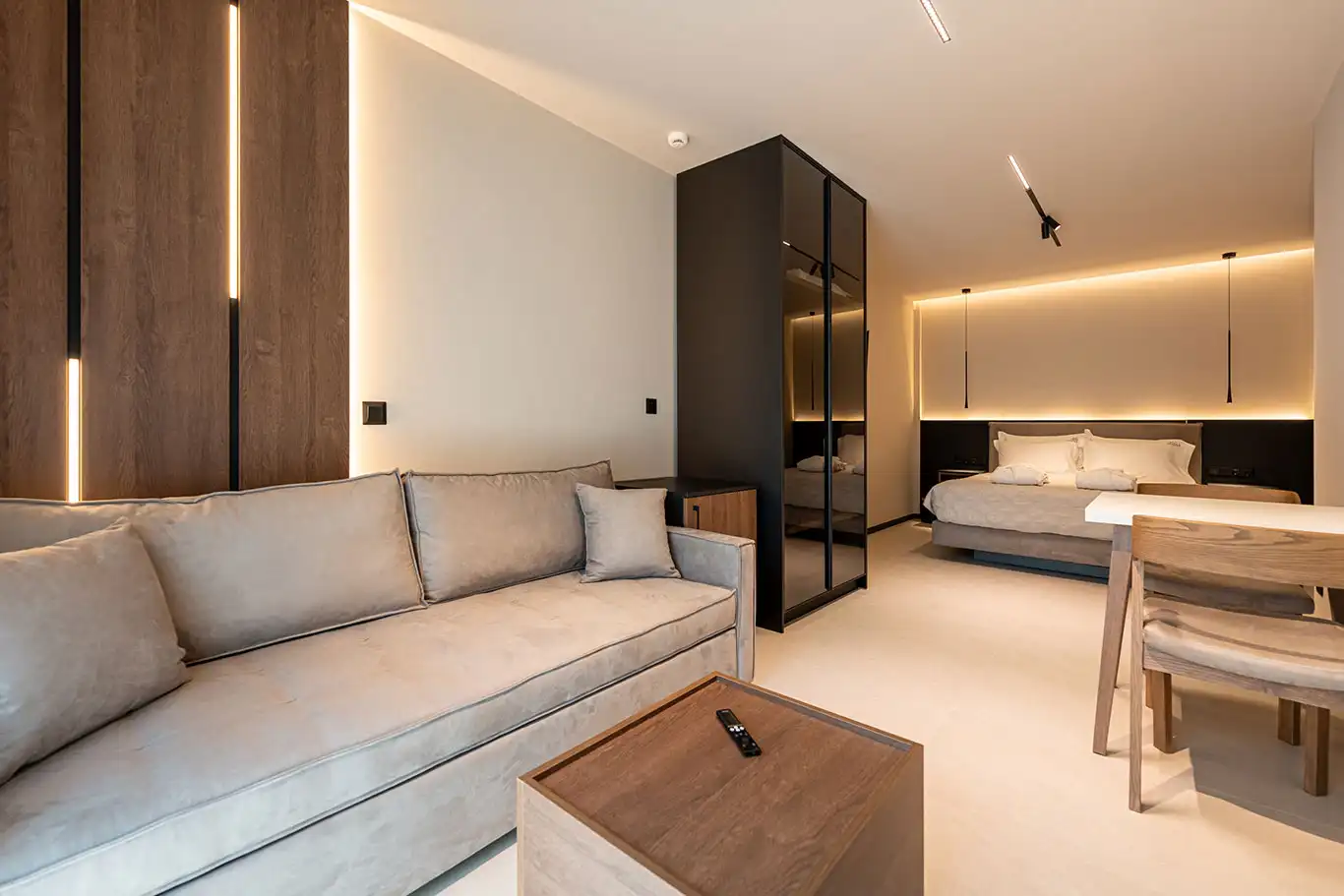Wide interior of Classic Luxury Room 106 with beige sofa, wooden coffee table, dining area, wardrobe and double bed