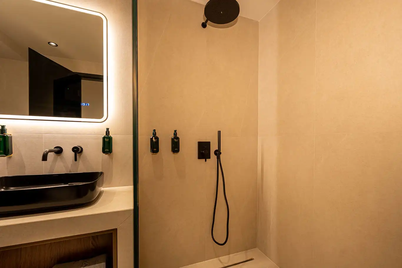 Glass walk-in shower with black rainfall showerhead, handheld shower and wall-mounted bathroom amenities