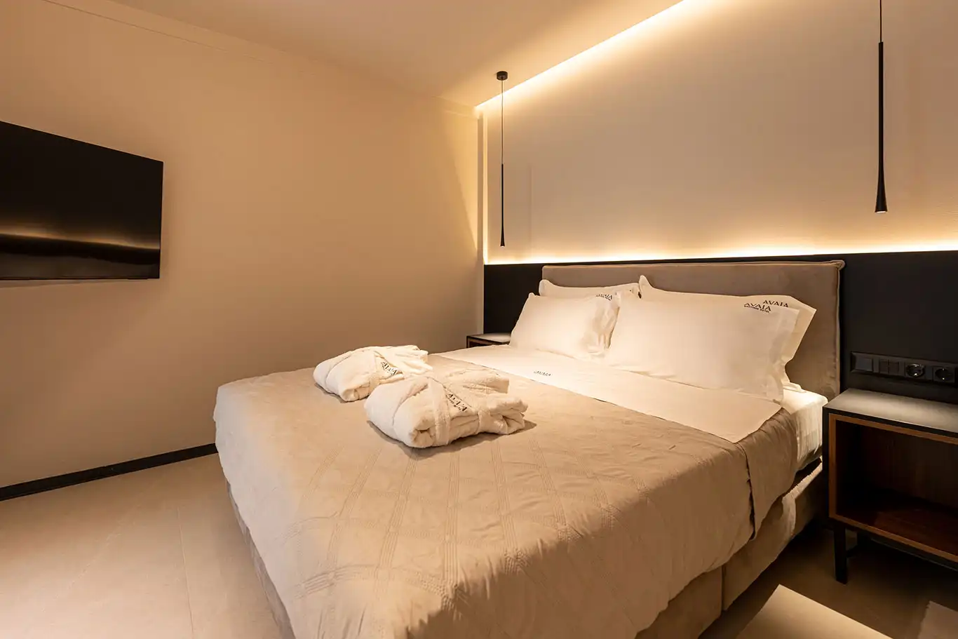 Bright double bedroom with white bedding, folded bathrobes, pendant lights and wall-mounted television