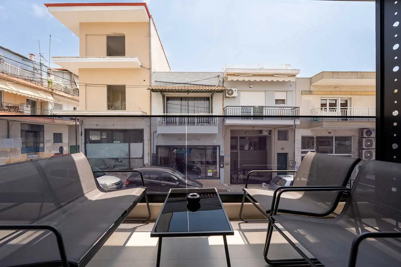 Front view of a private balcony with four outdoor chairs, a glass table and glass railing