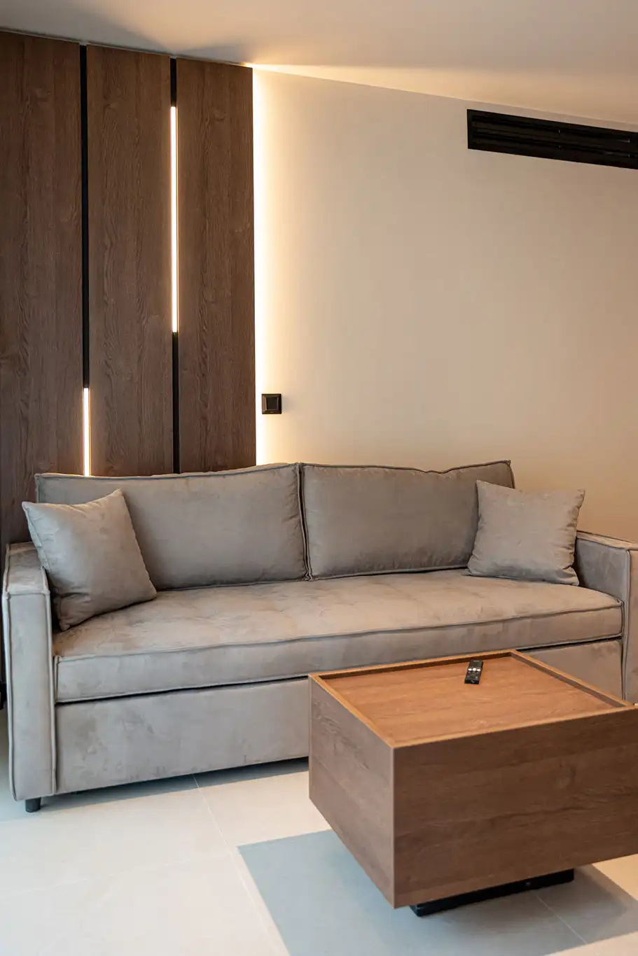 Grey sofa with decorative cushions, wooden coffee table and vertical ambient wall lighting