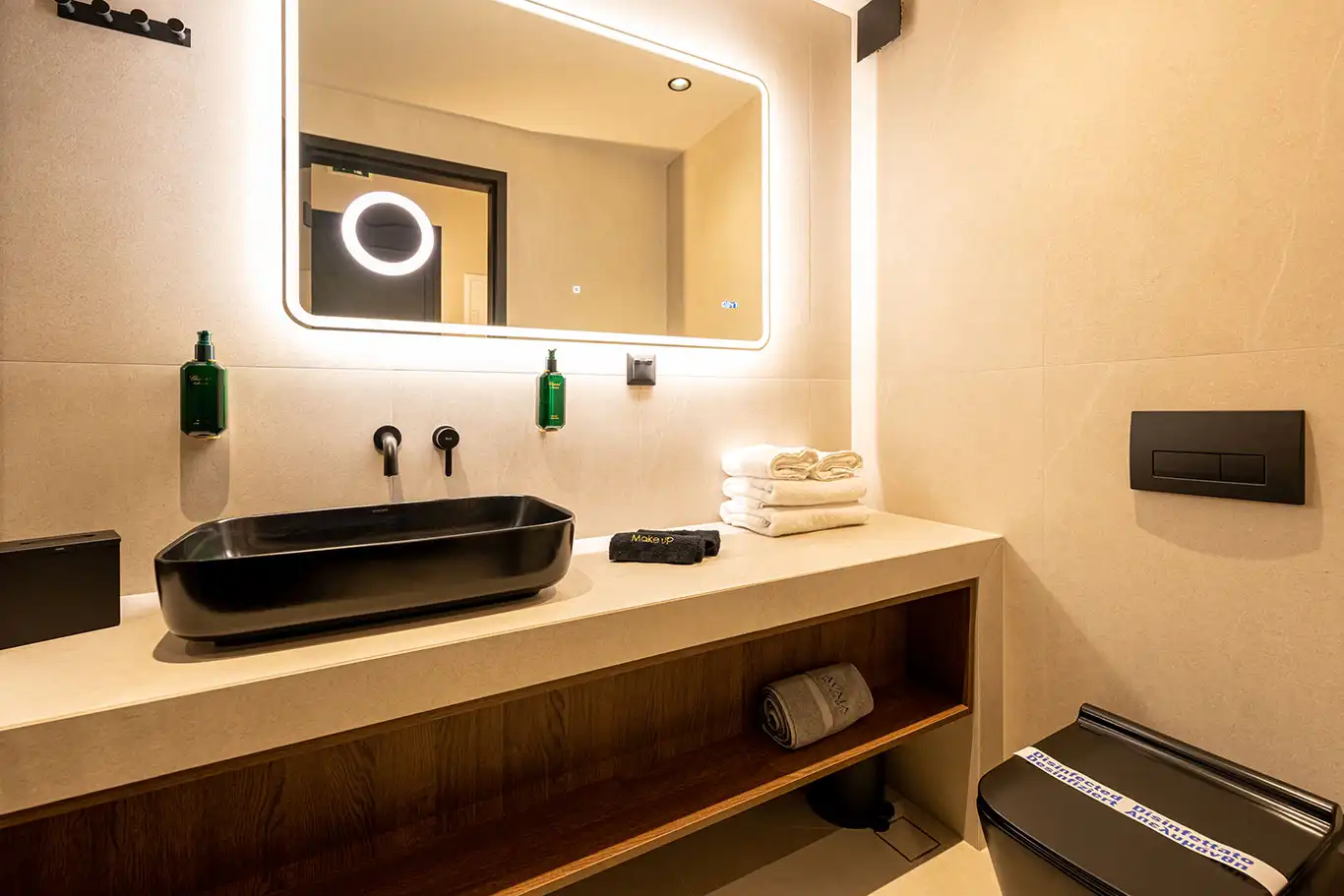 Modern bathroom with black basin, illuminated mirror, folded towels and black toilet