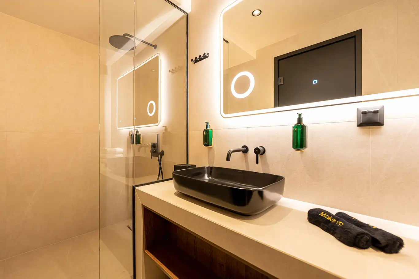 Modern bathroom with black countertop basin, illuminated mirror and glass walk-in shower