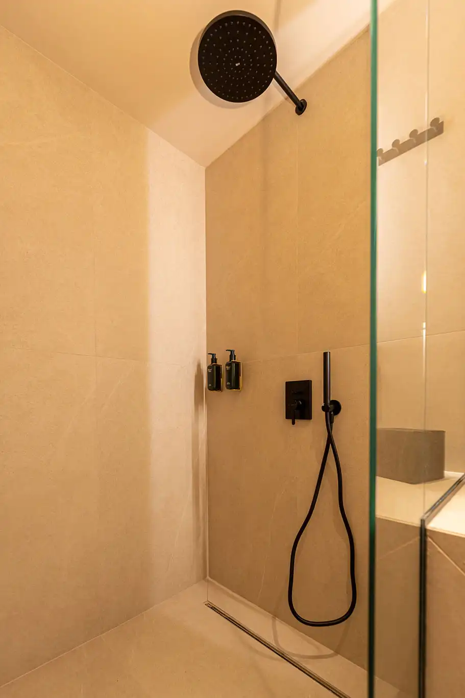Walk-in shower with large black rainfall showerhead, handheld shower and glass partition