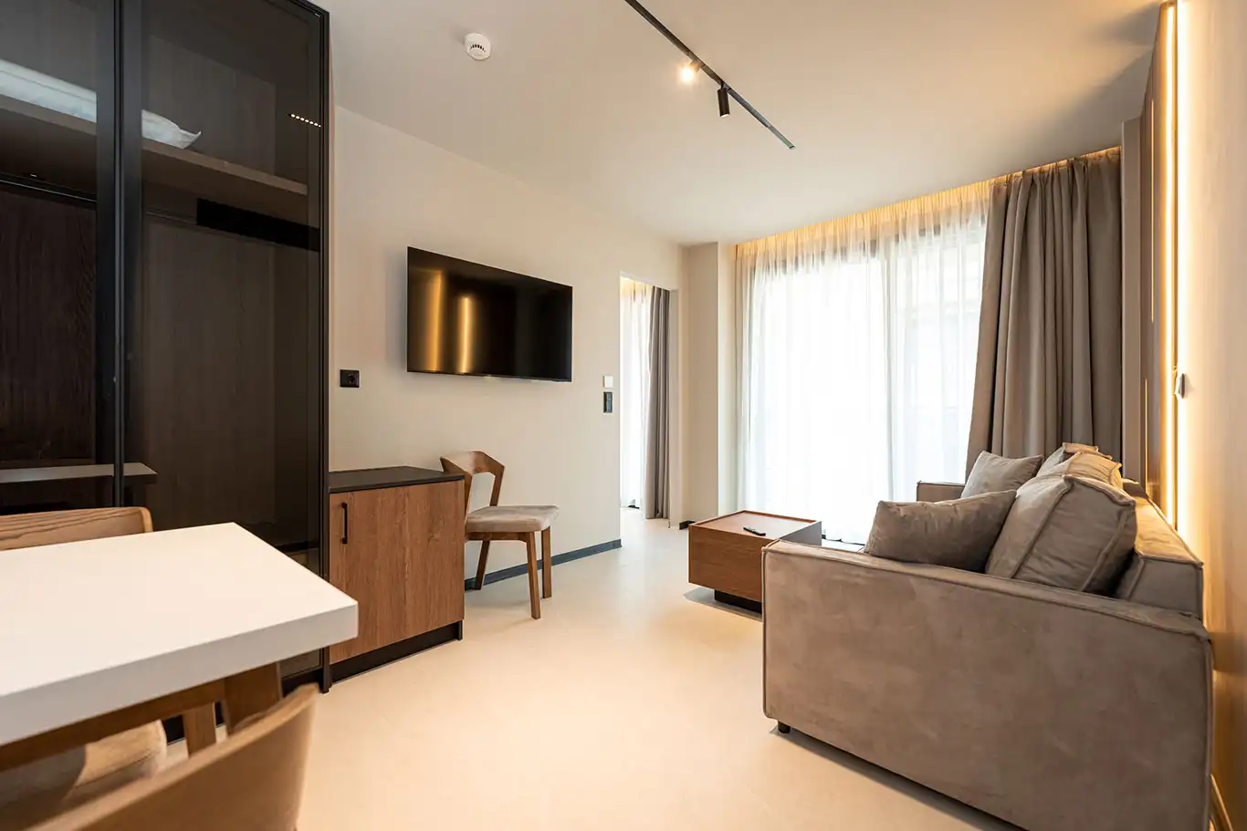 Open-plan living area with sofa, dining table, television, wardrobe and large balcony doors