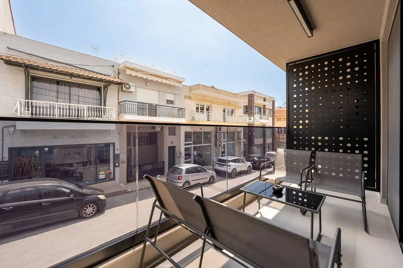 Private balcony with outdoor chairs, glass coffee table, glass railing and street outlook