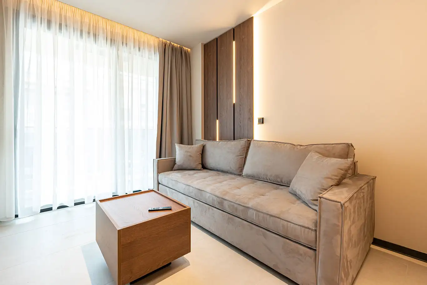 Spacious grey sofa beside a wooden coffee table and floor-to-ceiling curtains
