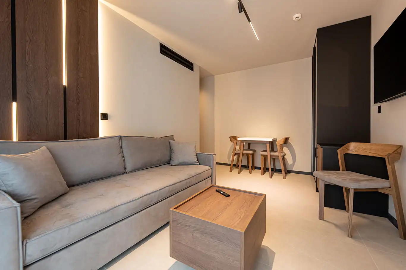 Modern living area with grey sofa, wooden coffee table, dining table and wall-mounted TV