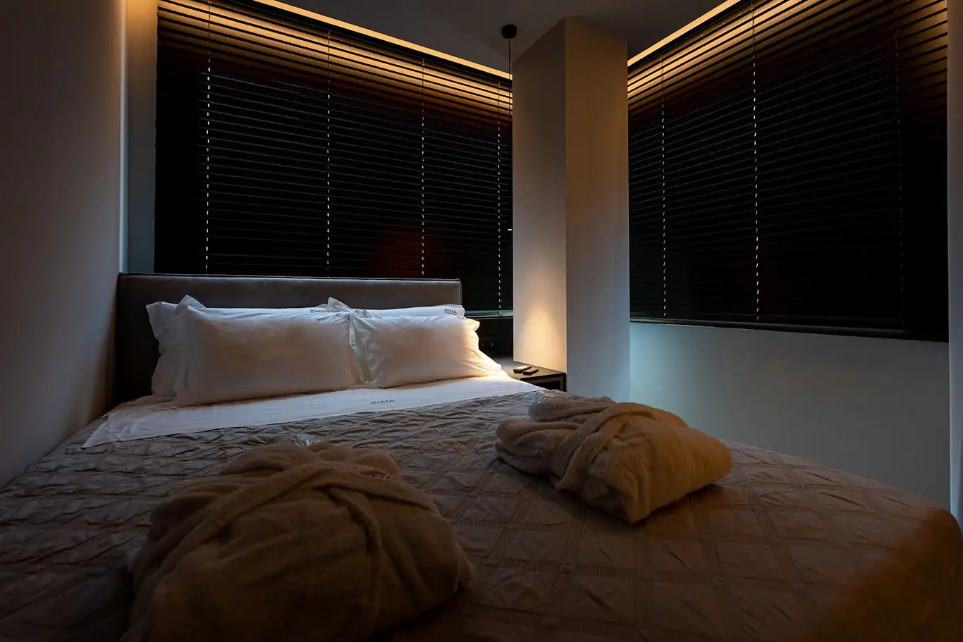 Double bed with white bedding, bathrobes and black blinds in Superior Luxury Room 102