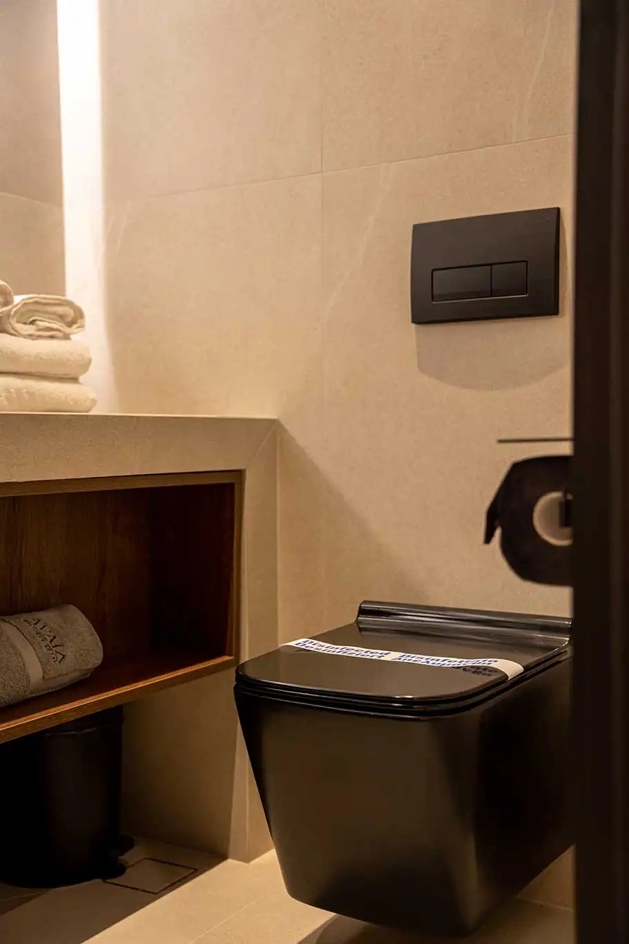 Black wall-mounted toilet beside a bathroom vanity with folded towels and open storage