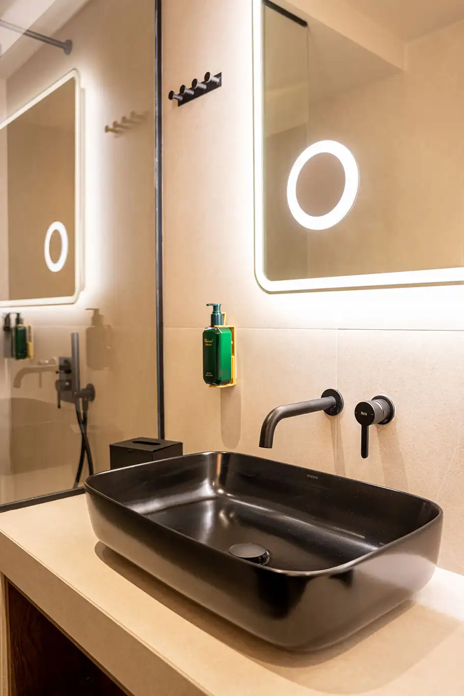 Close-up of a black countertop basin, wall-mounted tap and illuminated bathroom mirror