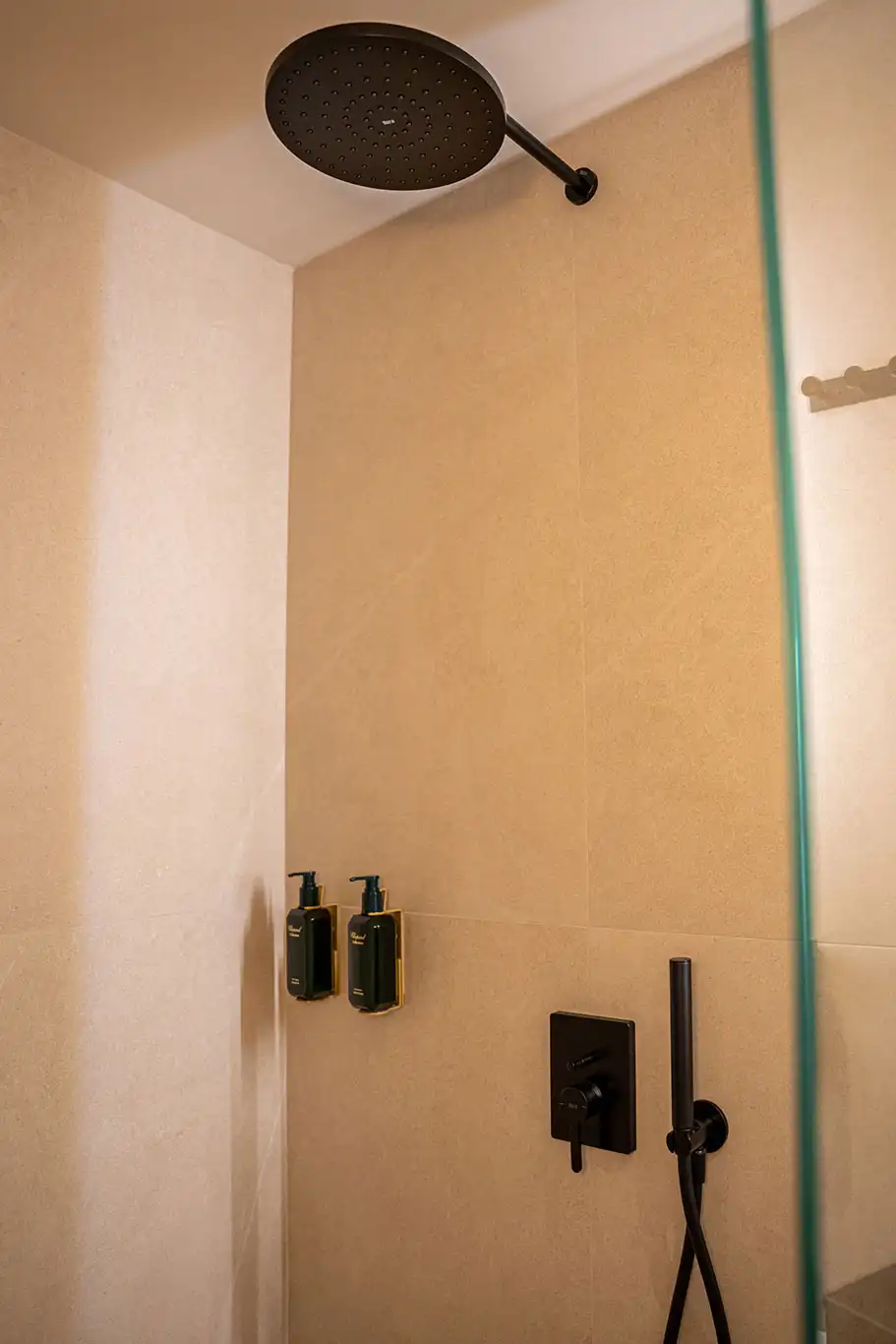 Close-up of a large black rainfall showerhead and handheld shower inside the walk-in shower