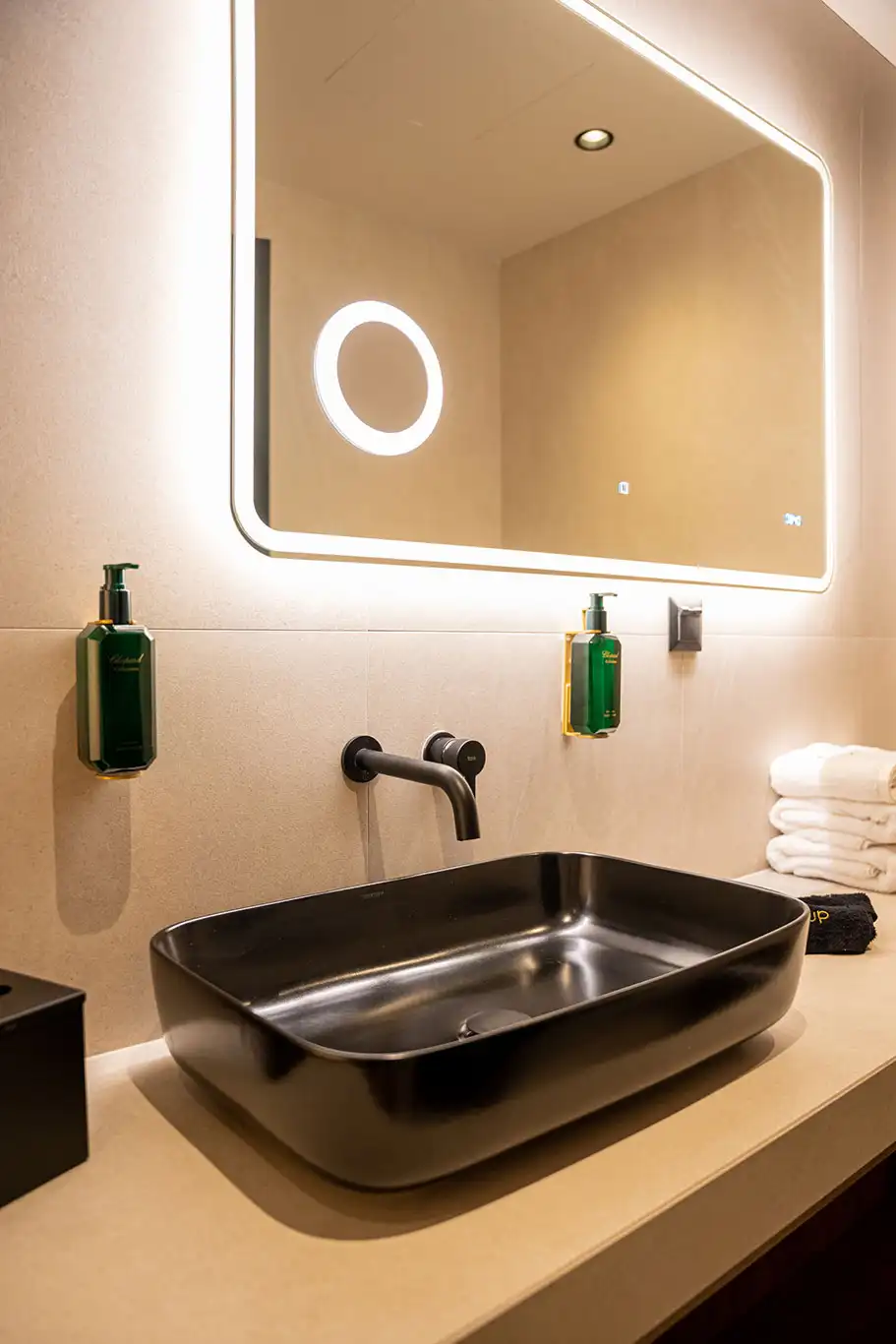 Close-up of a black rectangular bathroom basin beneath a large illuminated mirror