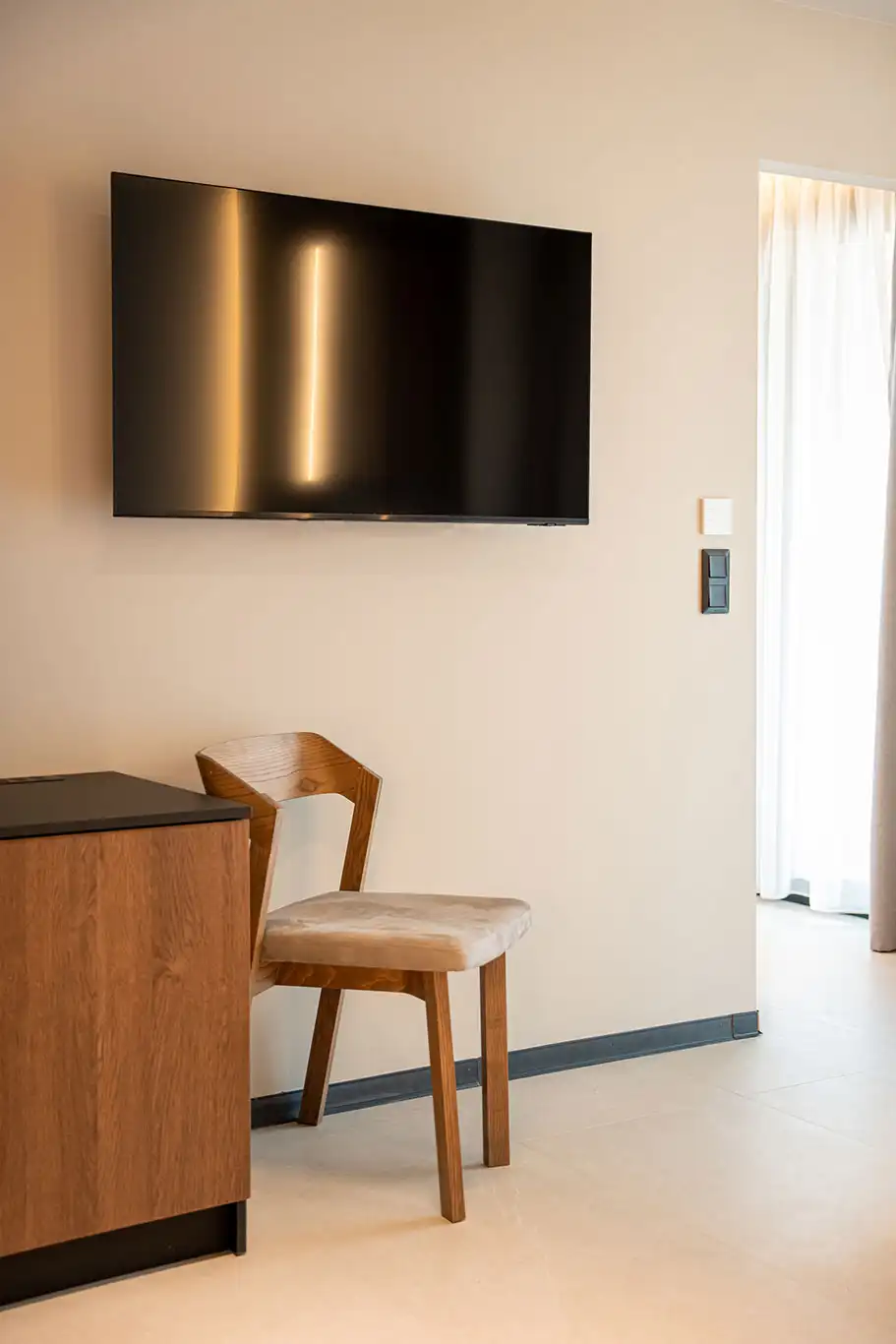 Wall-mounted flat-screen TV above a wooden cabinet and chair in the living area