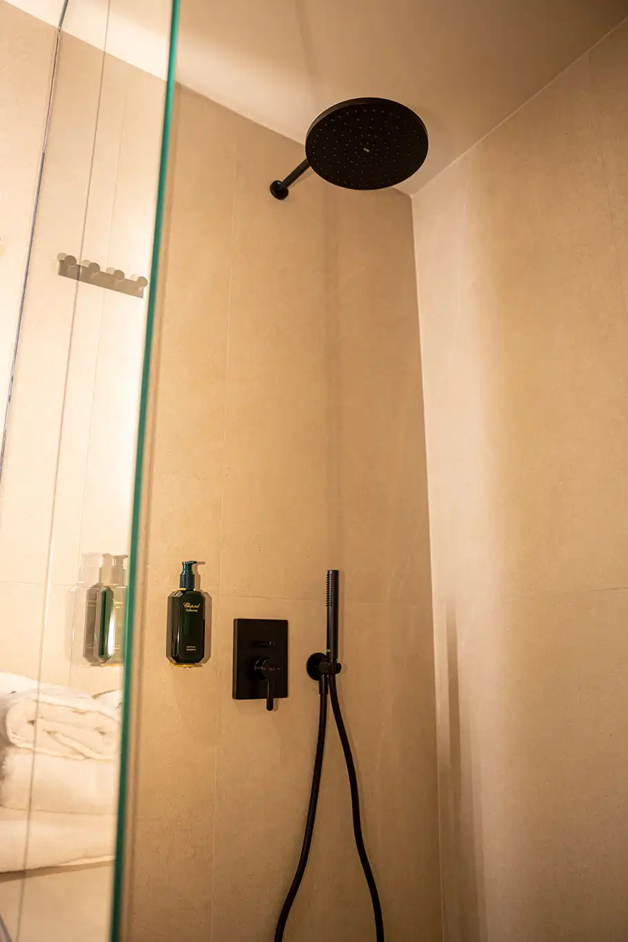 Glass walk-in shower with large black rainfall showerhead, handheld shower and wall-mounted amenities