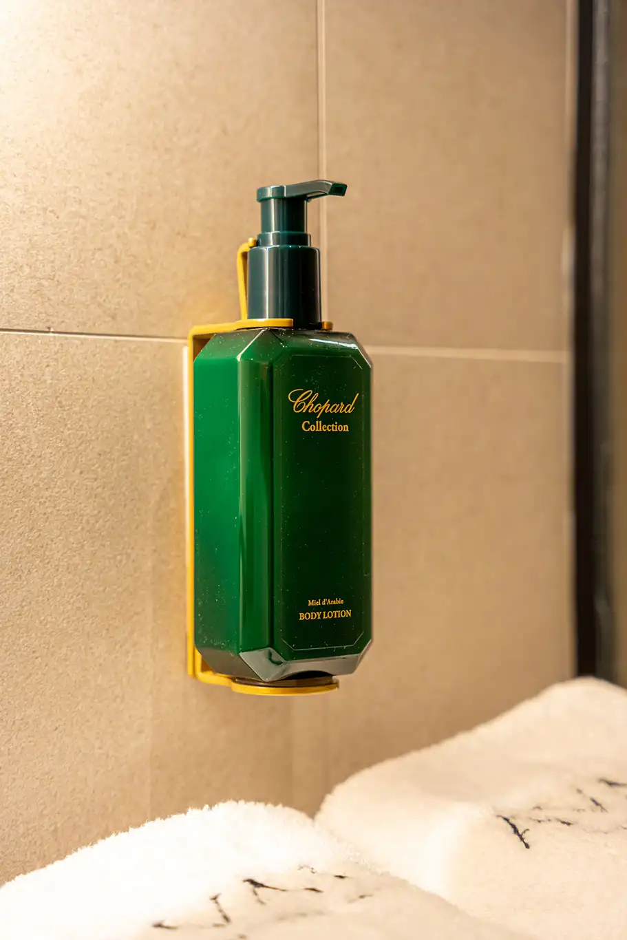 Close-up of a green Chopard Collection body lotion dispenser mounted on the bathroom wall