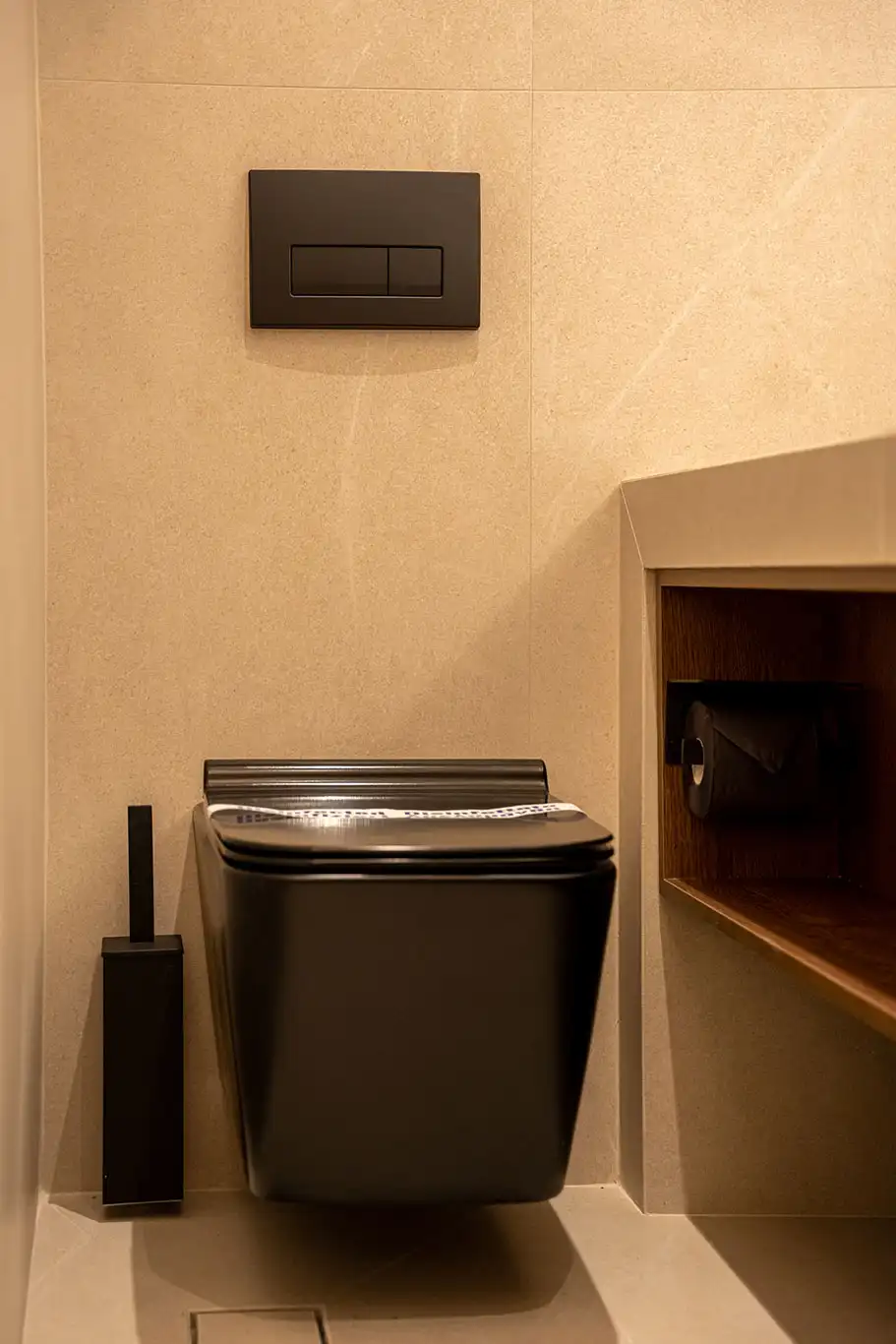 Black wall-mounted toilet with concealed flush plate, toilet brush and open bathroom storage