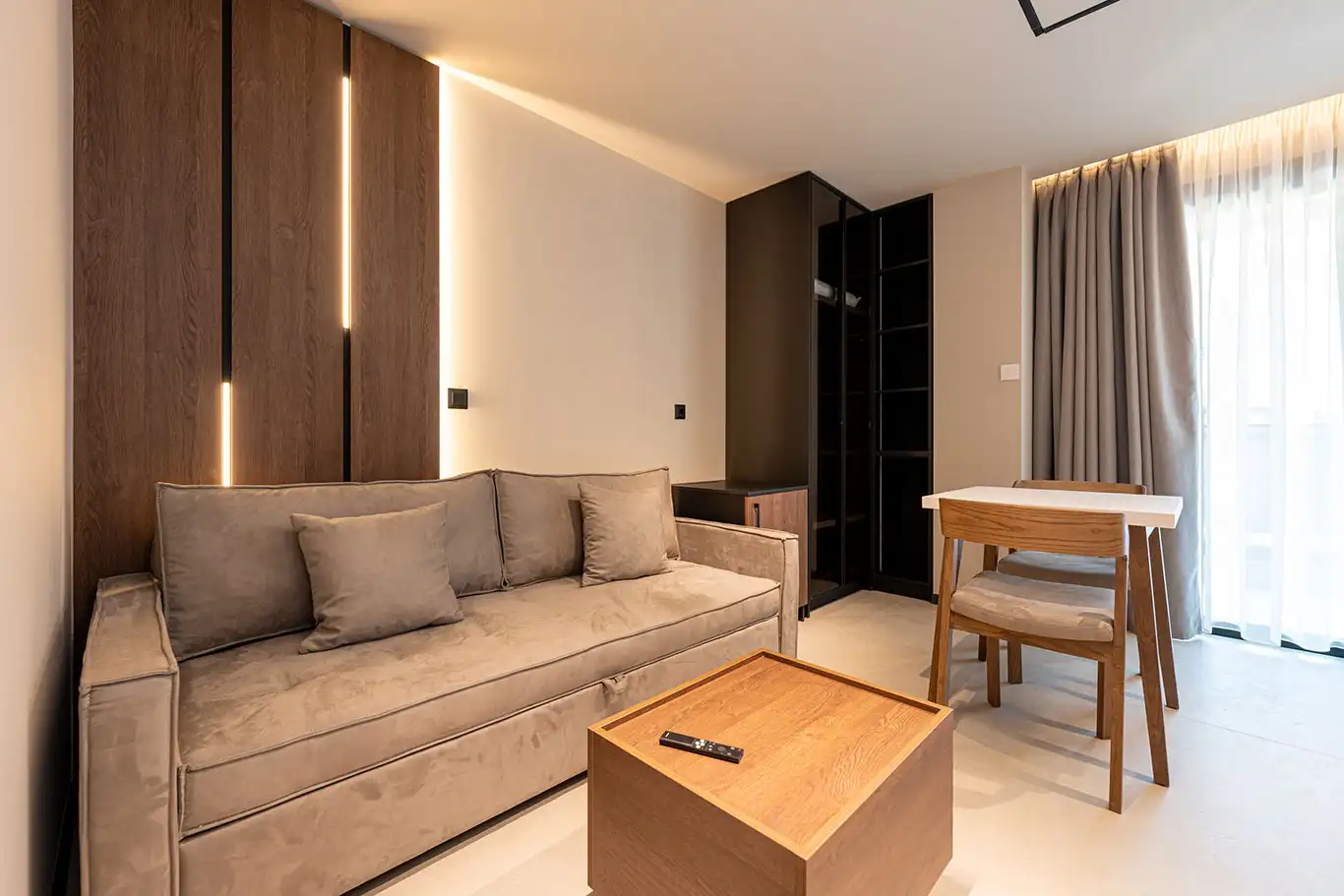 Modern living area with beige sofa, wooden coffee table, dining table, wardrobe and balcony doors