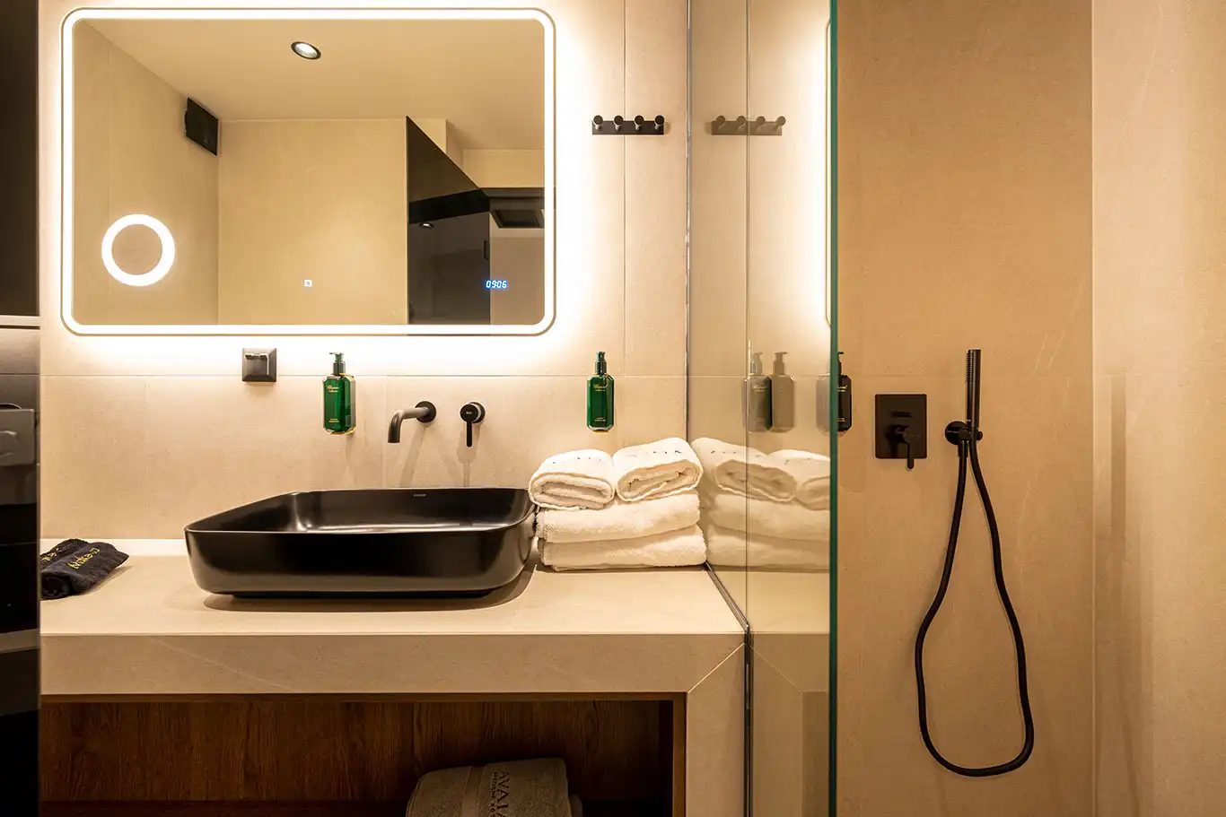 Bathroom with black countertop basin, illuminated mirror and glass walk-in shower with black fixtures