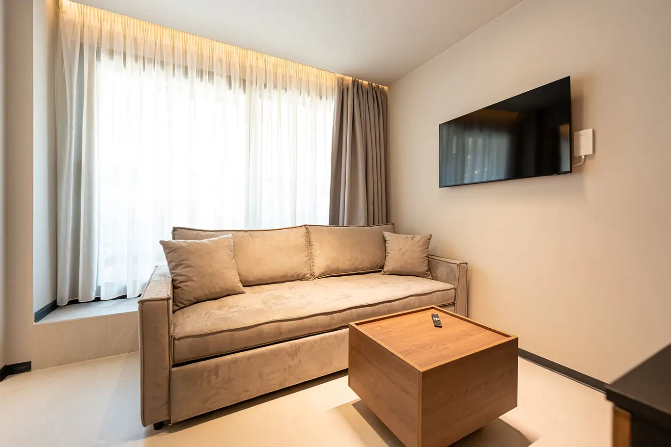 Comfortable sofa beneath a large window with a wall-mounted TV in Classic Luxury Room 101