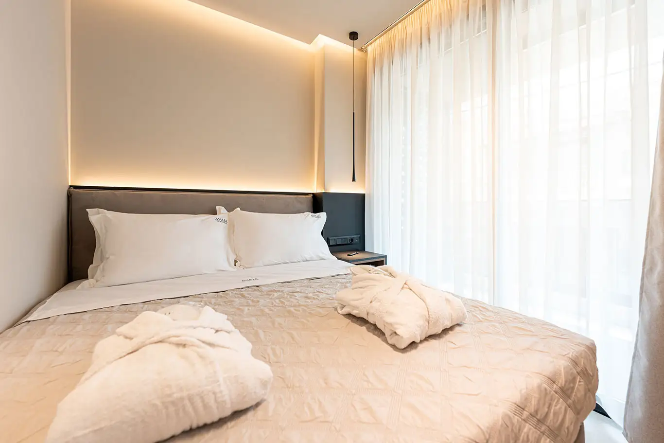 Double bed with bathrobes beside a large window in Classic Luxury Room 101 at Avaia Boutique Hotel